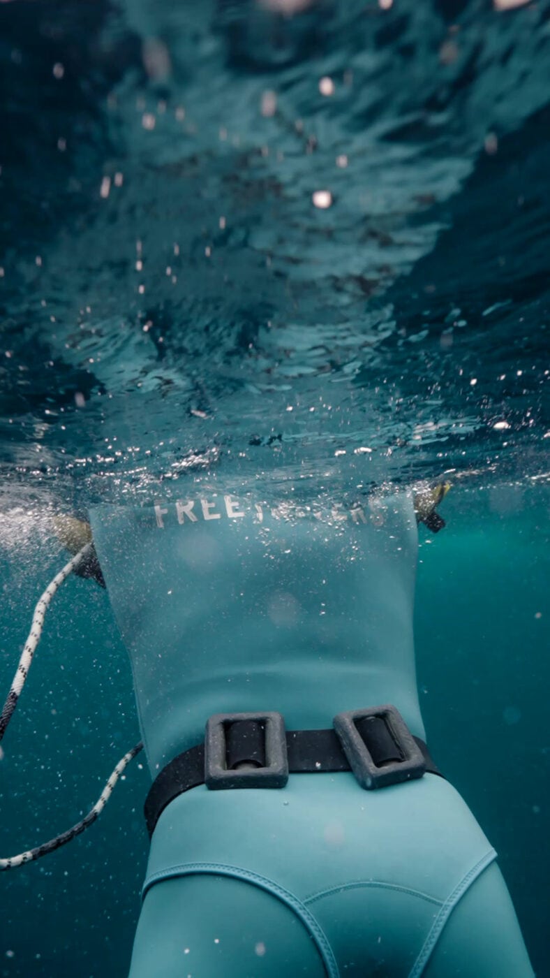 A relaxed freediver gliding at the surface in a teal wetsuit