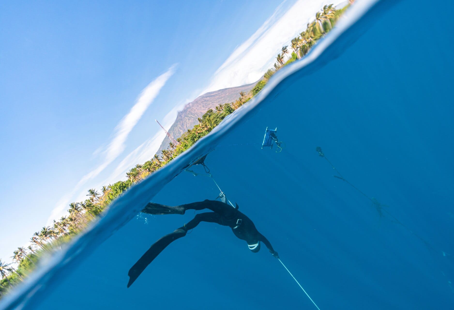 A freediver duck-diving down the line in clear water off the island