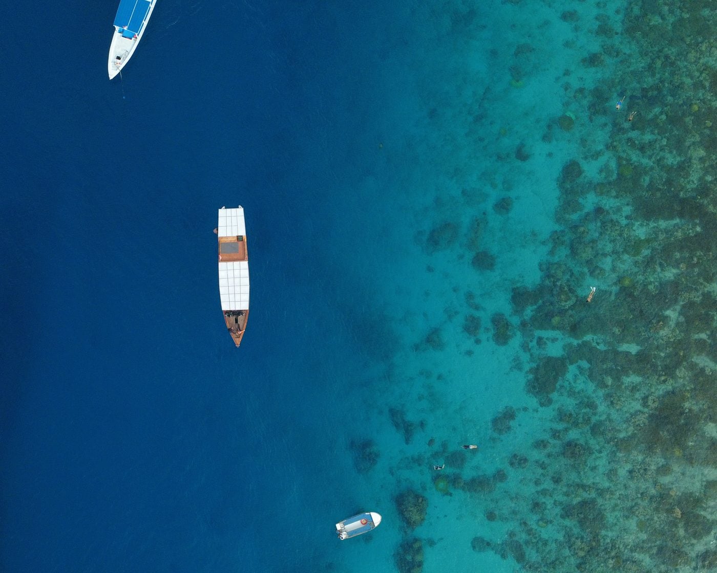 Dive boats moored over the turquoise reef off Gili Air, seen from above